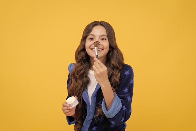 Happy child girl in cozy bathrobe grooming with powder brush skincare