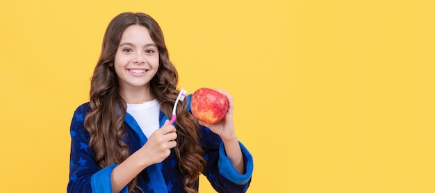 Happy child girl in cozy bathrobe use toothbrush and hold apple health Banner of child girl with teeth brush studio portrait header with copy space