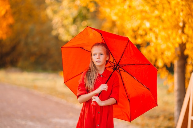 Happy child girl laughs under red umbrella