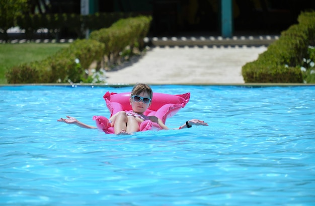 Happy child girl relaxing on inflatable air mattress in swimming pool on sunny summer day during tropical vacations Summertime activities concept