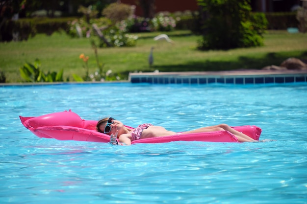 Happy child girl relaxing on inflatable air mattress in swimming pool on sunny summer day during tropical vacations Summertime activities concept