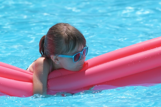 Happy child girl relaxing on inflatable air mattress in swimming pool on sunny summer day during tropical vacations Summertime activities concept