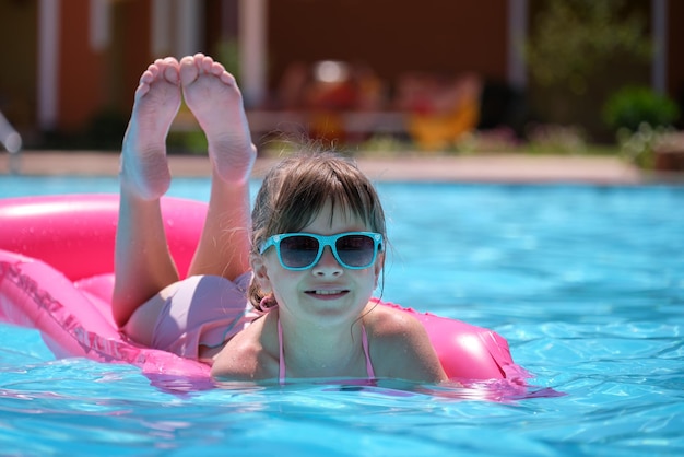 Happy child girl relaxing on inflatable air mattress in swimming pool on sunny summer day during tropical vacations Summertime activities concept