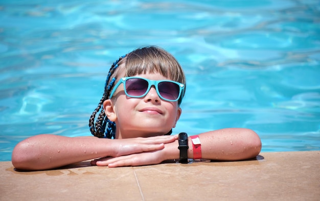 Happy child girl relaxing on swimming pool side on sunny summer day