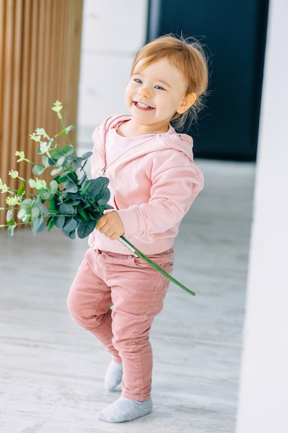 A happy child a girl running around the room holding a flower in her hands smiling