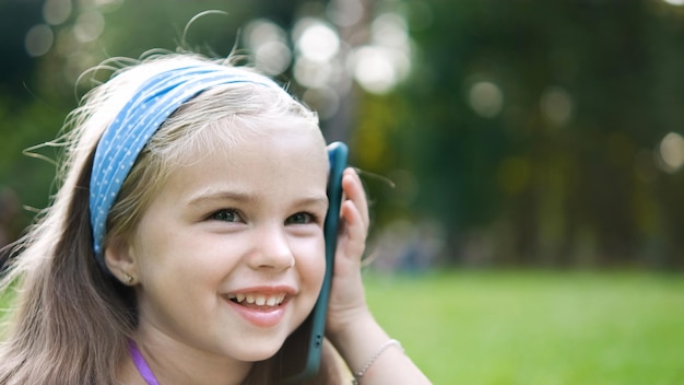 Happy child girl talking on mobile phone in summer park.