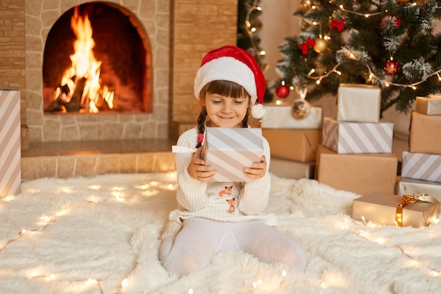 Happy child girl with christmas present at home sitting on warm carpet