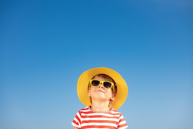 Happy child having fun outdoor against blue sky background. Portrait of smiling kid on summer vacation. Freedom and travel concept