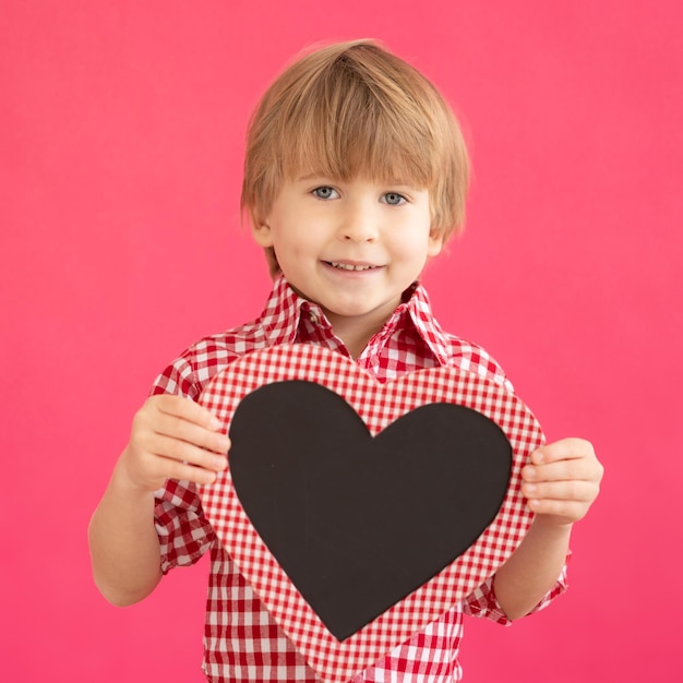 Happy child holding heart shaped blackboard blank