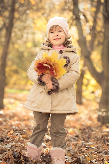 Happy child holding maple leaves in autumn park