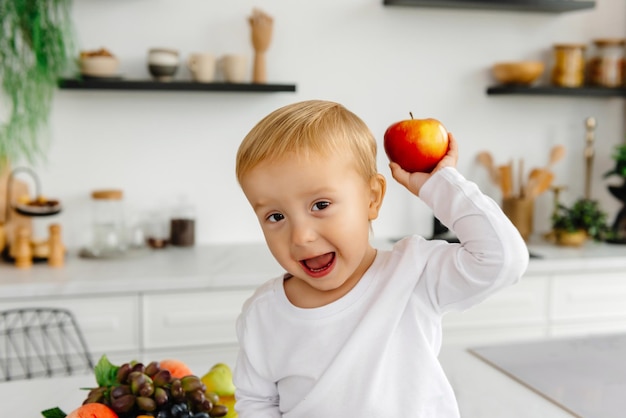 A happy child holding a red apple in his hand and waving to the camera