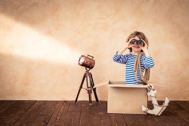 Photo happy child holding spyglass sitting on a vintage suitcase with a focus on a sailor theme background