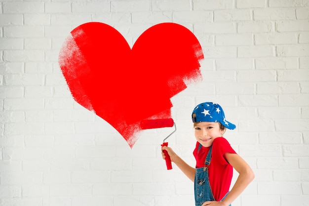 Happy child painting big red heart on the wall. Funny girl playing at home. Valentines day card. Renovation and design concept