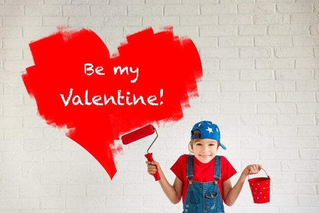 Happy child painting big red heart on the wall. Funny girl playing at home. Valentines day card. Renovation and design concept