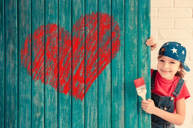 Happy child painting big red heart on the wall. Funny girl playing at home. Valentines day card. Renovation and design concept