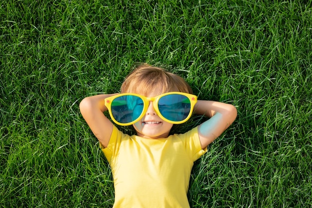 Happy child playing outdoor in spring park. Kid lying on green grass. Earth day and ecology concept. Top view portrait of boy outside