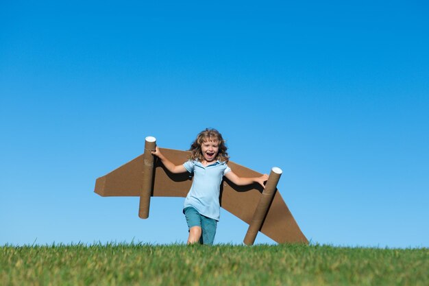 Happy child playing outside on green grass and blue sky kid pilot with toy jetpack kid boy play with...