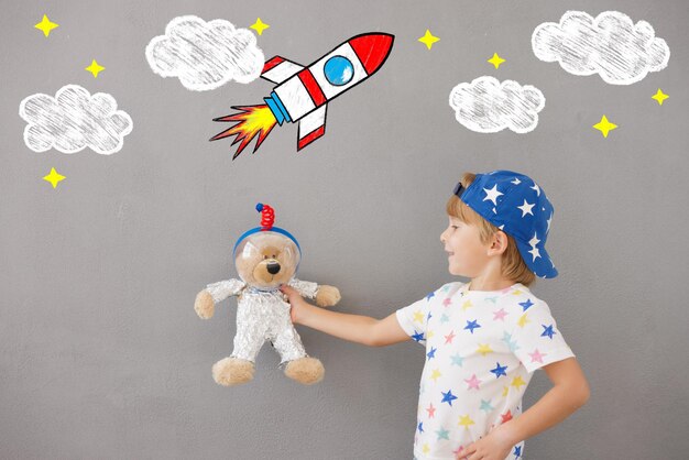 Photo happy child playing with teddy bear at home. kid pretend to be astronaut. imagination and children dream concept