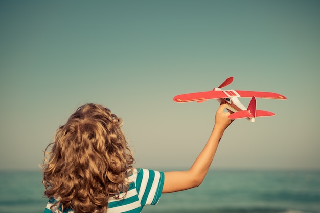 happy child playing with toy airplane against sea and sky on summer vacation