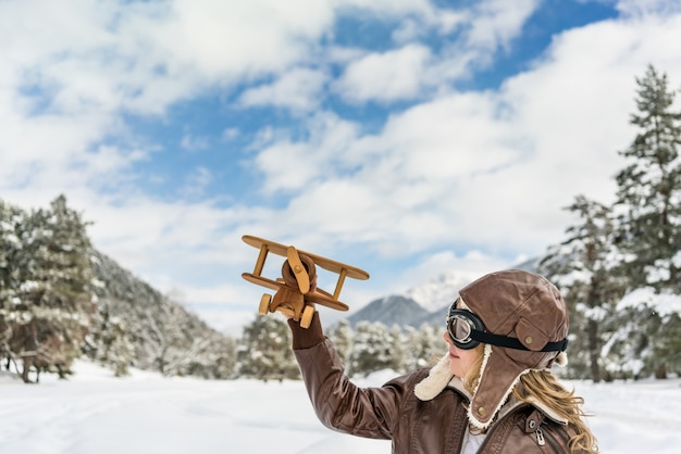 Happy child playing with toy airplane against winter sky background Kid pilot having fun outdoor