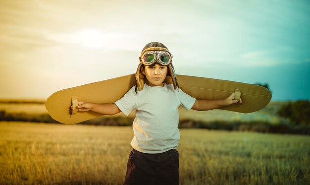 Photo happy child playing with toy wings against summer sky background. retro vintage toned. travel and adventure concept