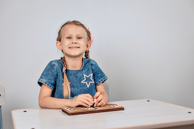 Happy child. Portrait of a smiling beautiful and radiant girl sitting at a white table in front of a puzzle and happily looking at the camera. Childhood happiness concept. photo with noise