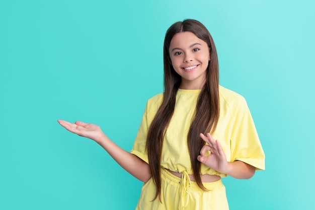 Happy child presenting product with ok gesture on blue background with copy space advertisement