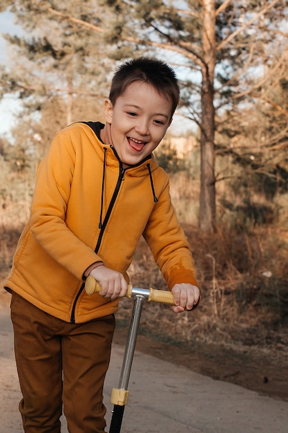 Happy child on a scooter in the park. Children learn to ride on roller boards. Active recreation for children on a safe residential street. Active sports for preschool children.