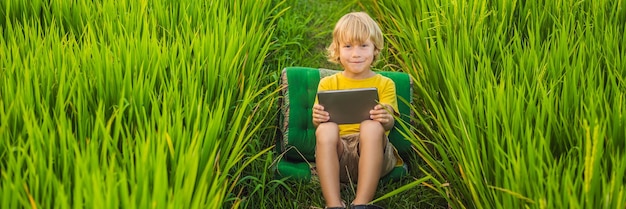 Happy child sitting on the field holding tablet boy sitting on the grass on sunny day home schooling