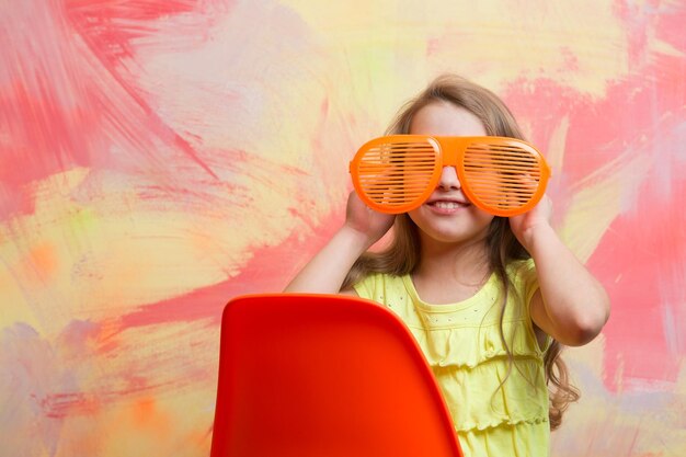 Happy child sitting on orange chair in summer glasses