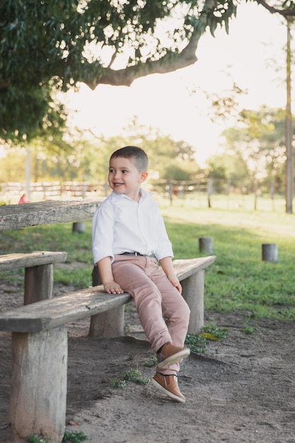 A happy child smiling in the field sitting on a wooden bench