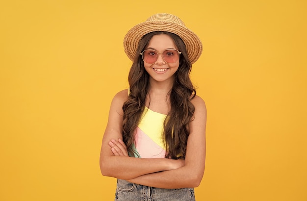 Happy child in summer straw hat and glasses has curly hair on yellow background beach fashion