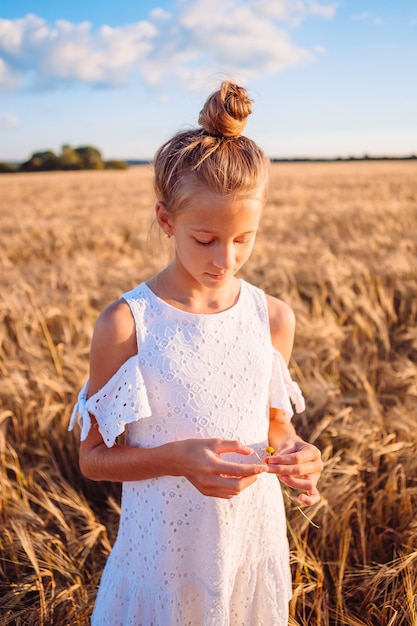 Happy child in wheat field. Beautiful girl in white dress in a straw hat with ripe wheat in hands