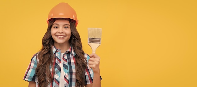 Happy child with curly hair in construction helmet hold painting brush painter Child builder 