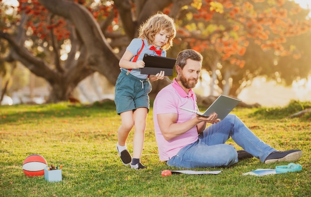 Happy child with father learning outdoor by studying online and working on laptop