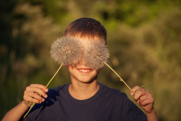 Happy child with fluffy dandelion eyes in a summer day. Boy is smiling, lifestyle