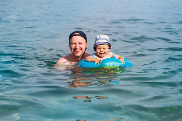 A happy child with his dad swims in a swimming ring in the blue sea