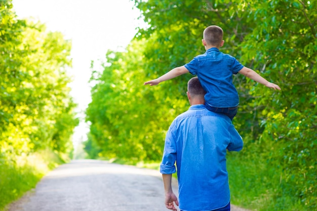 A Happy child with parent on shoulders walk along the road in park background