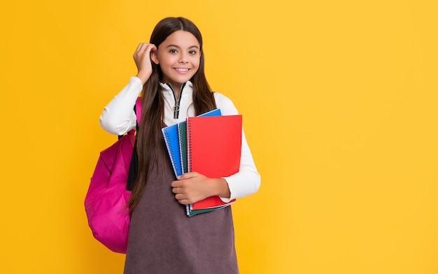 Happy child with school backpack and notebook on yellow background