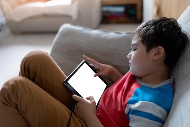 Happy Child with tablet computer Portrait Kid Holding Digital Tablet With Empty Screen Mockup Young boy sitting on sofa relaxing and playing with touch pad at home