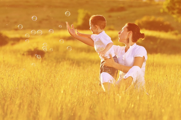 happy child and woman outdoor playing with soap bubble on meadow