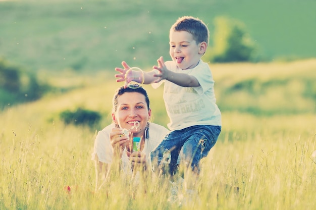 happy child and woman outdoor playing with soap bubble on meadow