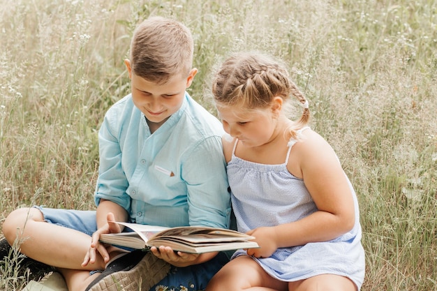 Happy children boy and girl reading the book under in summer on nature