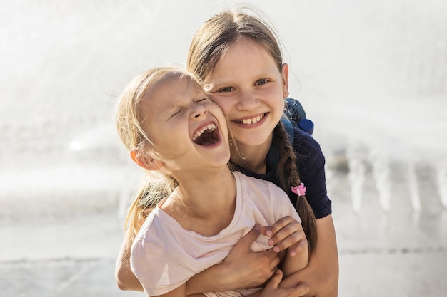 Happy Children have fun and hugging. Smiling Portrait of Emrbacing Girls Sisters in City Fountain