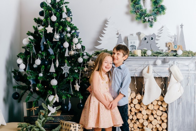 Happy children hugging and laughing in studio with cristmas tree and winter holidays decorations.