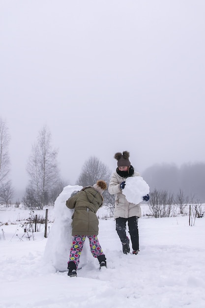 Happy children make a snowman in a snow-covered field in the countryside.