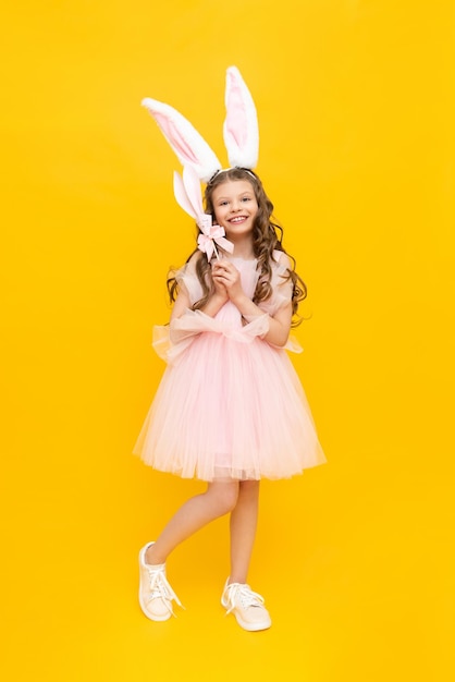 Happy children's Easter A curlyhaired girl dressed in an Easter bunny An extraordinarily beautiful teenage girl with long ears and a lush dress on a yellow isolated background