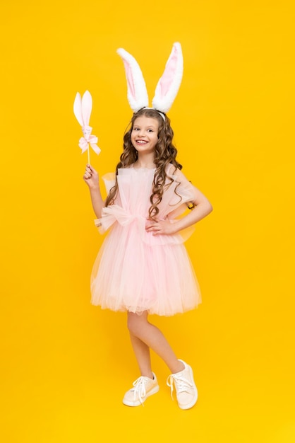 Happy children's Easter A curlyhaired girl dressed in an Easter bunny An extraordinarily beautiful teenage girl with long ears and a lush dress on a yellow isolated background