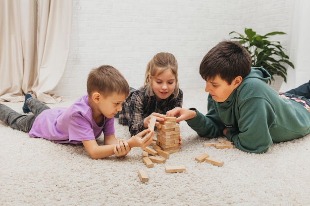 Happy children sit on the floor and play an educational game (jenga) and stand in a tower of blocks