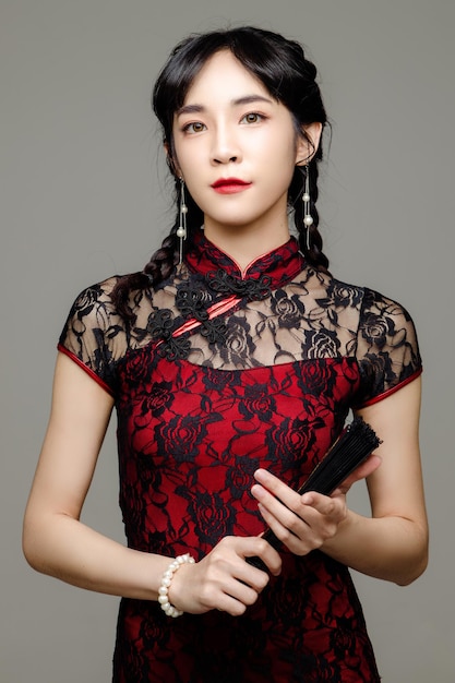 Happy Chinese new year Asian woman wearing modern cheongsam dress holding a fan in hand